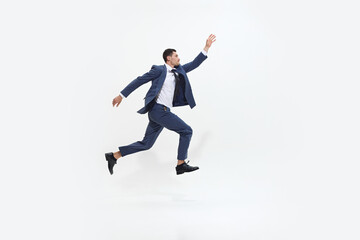 Man in suit runs energetically with determined expression, in mid-air as if striving towards something against white studio background. Concept of DEI, business, partnership, work, support and unity.