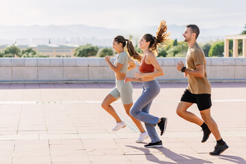 Side view of three young athletic friends jogging together outdoors in summer. Healthy lifestyle and sport concept