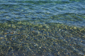 Clear blue water gently laps over a bed of smooth pebbles