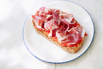 Close-up of a single slice of toasted bread and thinly sliced ​​serrano ham