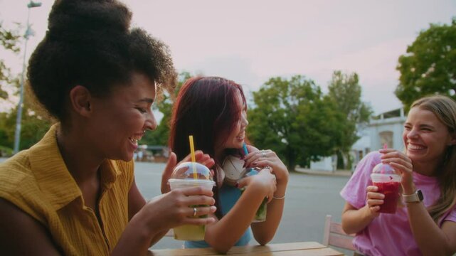 Three cheerful girlfriends toasting with drinks by table