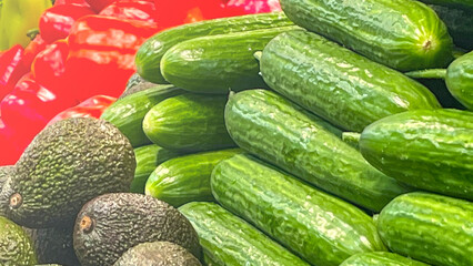 A pile of cucumbers and avocados. The cucumbers are stacked on top of each other
