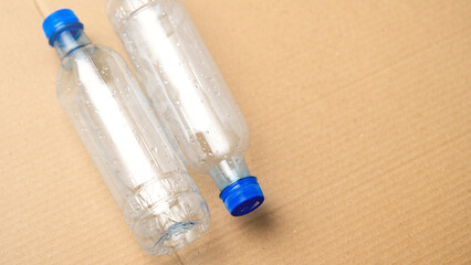 Naklejka premium Two plastic bottles with blue caps on a brown surface. The bottles are empty and appear to be discarded