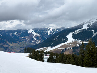 Scenic view of ski region of Saalbach-Hinterglemm and slopes in bad conditions in the Austrian alps against cloudy sky in mid March 2024