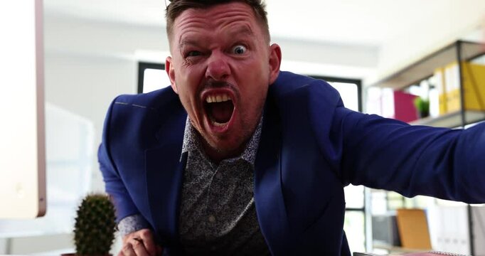 Angry businessman screaming and pointing at camera in office. Portrait of aggressive boss scolding and yelling at employees