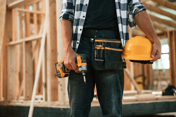 Orange colored drill and hardhat in hands. Industrial worker in wooden warehouse