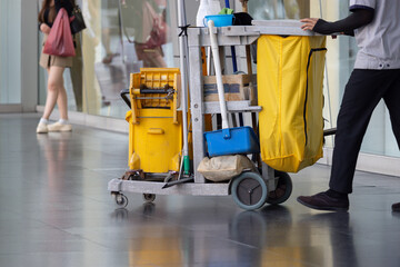 A man in a uniform is pushing a cart with cleaning supplies