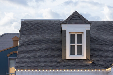 A house with a slanted roof and a window on the top. garret house with roof shingle in evening.