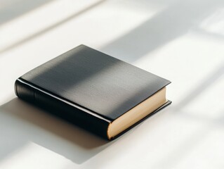 A simple black book lies on a surface, illuminated by soft natural light, casting gentle shadows.