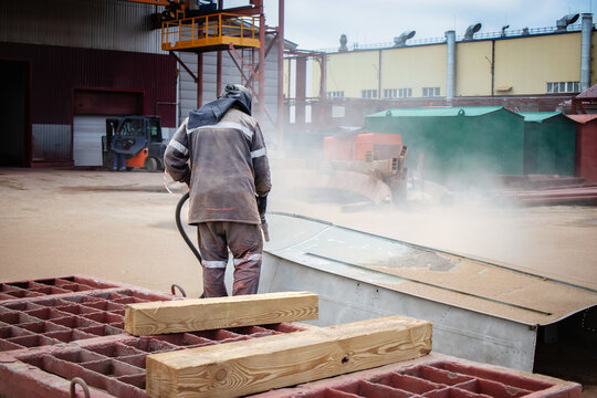 A worker sandblasting a metal structure to remove rust at an industrial plant on a cloudy day - Powered by Adobe
