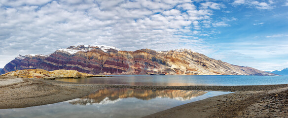 Segelsallskapet panorama with reflection. A tail ship is anchored in the clear blue fjord, with the...