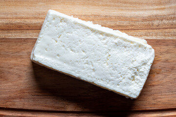 Block of raw uncut cottage cheese or Indian paneer on wooden chopping board