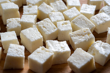 Block of raw cottage cheese or Indian paneer cut into small cubes on wooden chopping board. Selective focus.