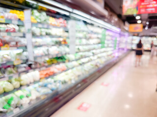 Blurred view of a grocery store aisle with brightly lit refrigeration shelves filled