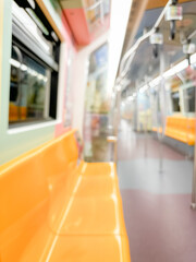 Blurred interior of an empty subway train with yellow seats, stainless steel poles, and overhead handles..