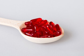 Vitamin capsules in a spoon on a colored background. Pills served as a healthy meal. Red soft gel...