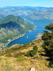 High Angle View of Bay of Kotor Surrounded by Rocky Mountains in Montenegro, Featuring Clear Blue Waters, Green Hills, Coastal Villages, and Boats on a Bright Sunny Day