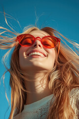 A woman with long blonde hair and red sunglasses is smiling