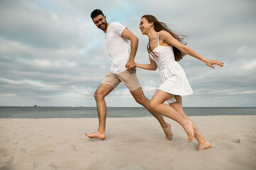 Young couple in love, laughing, running on the beach on the sand, holding hands
