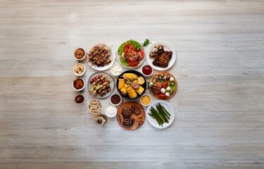 A tabletop spread of grilled food arranged on white plates and bowls, with a white wooden background.