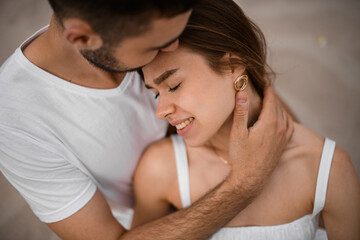 Fototapeta premium Close-up of young woman and man in love, smiling bride closes her eyes with pleasure and leans her head on his shoulder