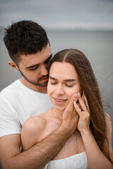 Fototapeta premium Man cups a woman's face with his palm, standing behind her and hugging her shoulders, and she gently touches his palm in return