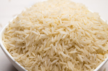 Raw basmati rice, in white bowl, on light wooden surface.