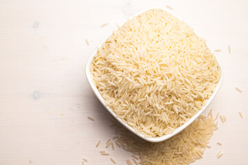 Raw basmati rice, in white bowl, on light wooden surface.