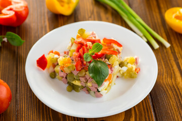 vegetable salad of boiled vegetables, with peas, sausage, sweet pepper. On a wooden table