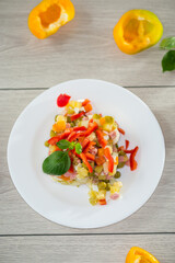 vegetable salad of boiled vegetables, with peas, sausage, sweet pepper. On a wooden table