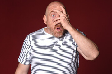 adult man showing a sign of surprise with hand on face in red background