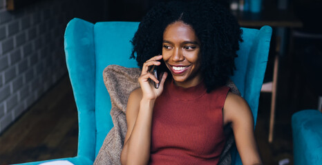 Cheerful female copywriter smiling during positive friendly smartphone conversation during remote...