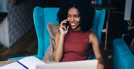 Cheerful female copywriter smiling during positive friendly smartphone conversation during remote...