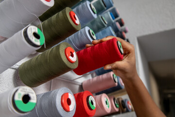 Anonymous seamstress selecting colored threads for sewing in a fabric studio