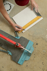 Woman doing measurements and cutting tiles with a standard manual tile cutter. Process of installation of tiles in the bathroom step by step. DIY home improvement.