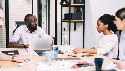 Multicultural team of male and female professionals dressed in formal wear discussing strategy and solution during working process and briefing in modern office, diverse experienced business people