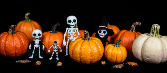 group white skeletal figures stand amongst pumpkins on a black surface