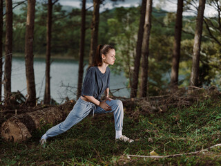 Focused young woman stretching outdoors in a natural setting, wearing casual athletic clothing near a serene lake, emphasizing fitness and well being