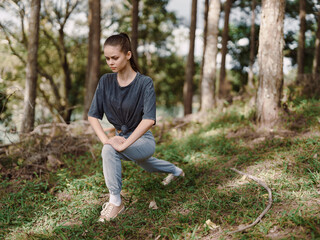 Obraz premium Active young woman performing lunges in a forest setting, wearing casual sportswear Fitness and wellness concept in nature