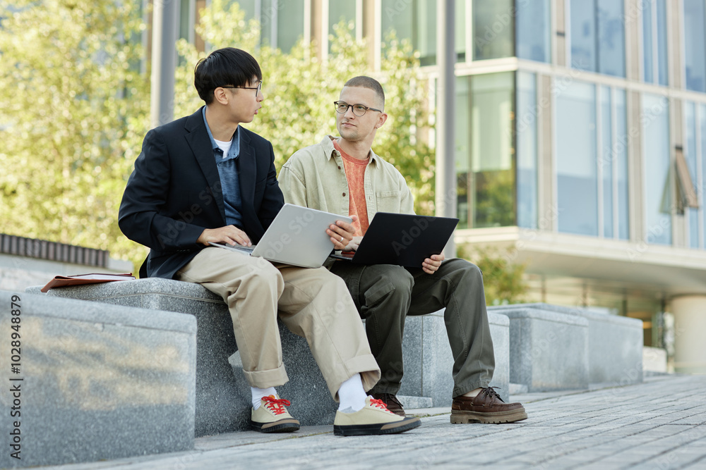 Poster full shot of male it programmer with buzz cut in conversation with colleague using laptop to write c