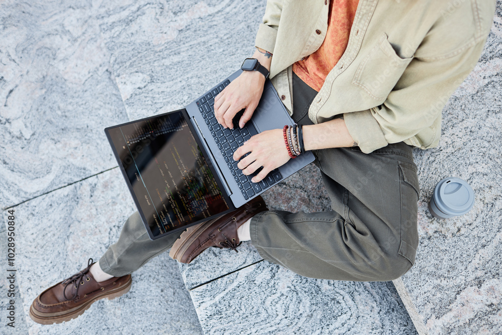 Poster high angle of unrecognizable male it developer using laptop to write code sitting on concrete steps 