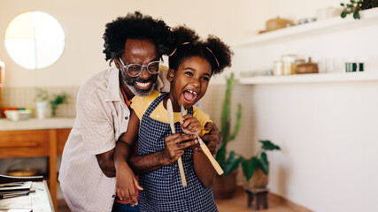 Cheerful afro-haired father and daughter bonding in brazilian kitchen, having fun with wooden spoons