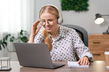 Interpreter in headphones working with laptop at table indoors