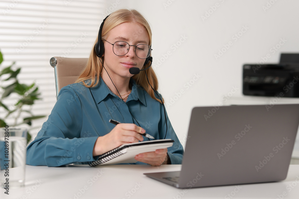 Poster interpreter in headset taking notes while working with laptop at table indoors