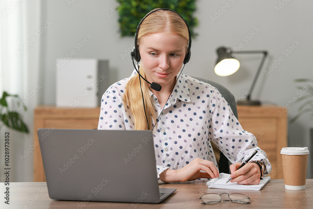 Poster interpreter in headset taking notes while working with laptop at table indoors