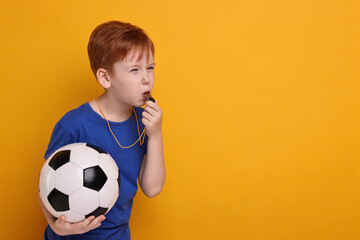 Little boy with soccer ball blowing whistle on orange background, space for text