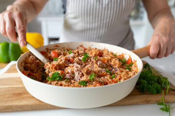 Homemade food with a fresh cooked and healthy meal with rice, vegetables and tuna in a pan in the kitchen. Prepared by a woman with apron