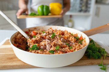 Homemade food with a fresh cooked and healthy meal with rice, vegetables and tuna in a pan in the kitchen. Prepared by a woman with apron