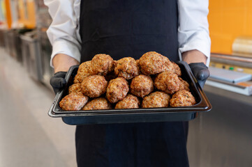 The cook's hands in black gloves hold a tray of fried cutlets in a supermarket, his own production....