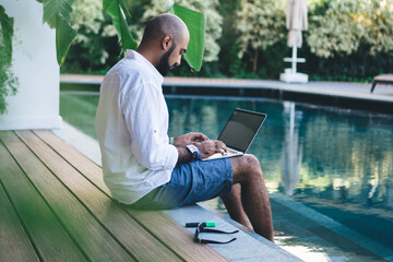 Man with laptop on edge of pool